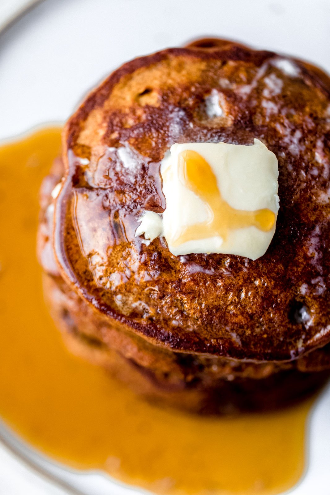 Tortitas de pan de jengibre increíblemente esponjosas hechas con harina de trigo integral, especias calientes y melaza dulce perfecta. Estos panqueques de pan de jengibre más saludables no contienen productos lácteos y están perfectamente condimentados, ¡oh, tan esponjosos, el brunch navideño perfecto! Vista desde arriba de una pila de panqueques de jengibre con mantequilla y jarabe de arce