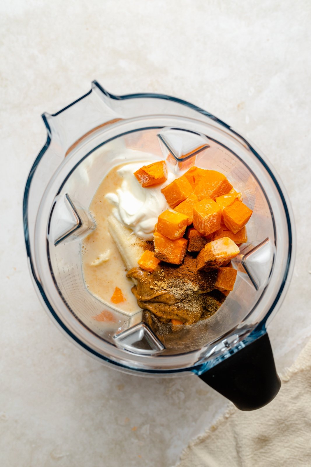¡El cremoso y delicioso Batido de Calabaza Butternut está lleno de maravillosos y reconfortantes sabores de la especia chai! Repleto de proteína y fibra, esta receta de batido de calabaza no contiene lácteos y es el desayuno o merienda nutritivo perfecto. Vista de arriba hacia abajo de los ingredientes en la licuadora de batidos de calabaza