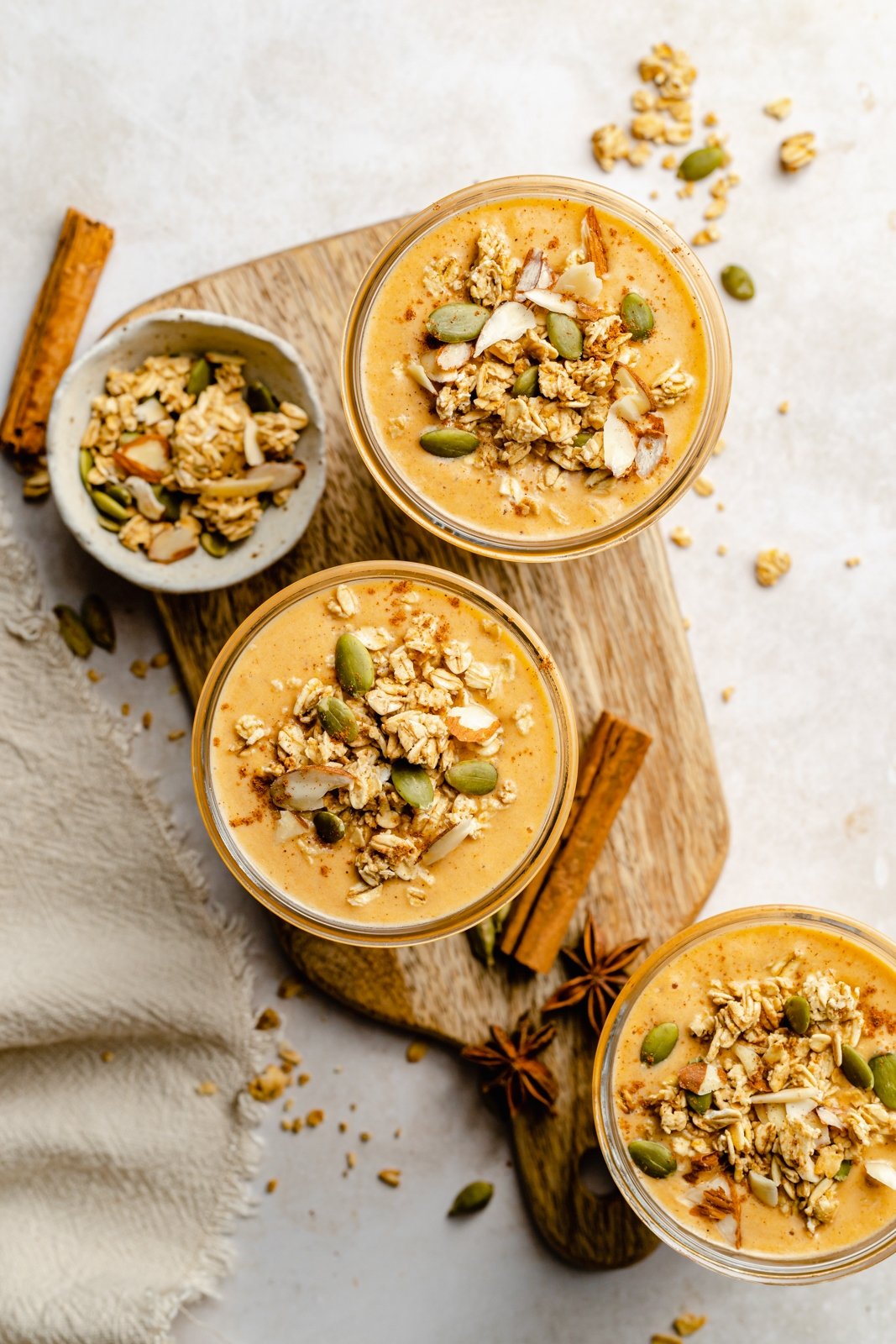¡El cremoso y delicioso Batido de Calabaza Butternut está lleno de maravillosos y reconfortantes sabores de la especia chai! Repleto de proteína y fibra, esta receta de batido de calabaza no contiene lácteos y es el desayuno o merienda nutritivo perfecto. Vista superior de tres batidos de calabaza con granola