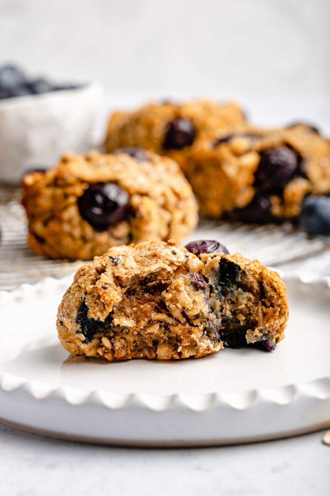 ¡Un plato de galletas de desayuno de arándanos veganas y sin gluten que saben igual que muffins de arándanos! Estas saludables galletas de desayuno de arándanos son naturalmente dulces y están llenas de nutrientes de semillas de chía, lino, avena, nueces y más ingredientes. Perfectas para congelar, ¡Es el desayuno o merienda perfecto para las semanas ocupadas! Galletas de desayuno de arándanos en un plato con un bocado