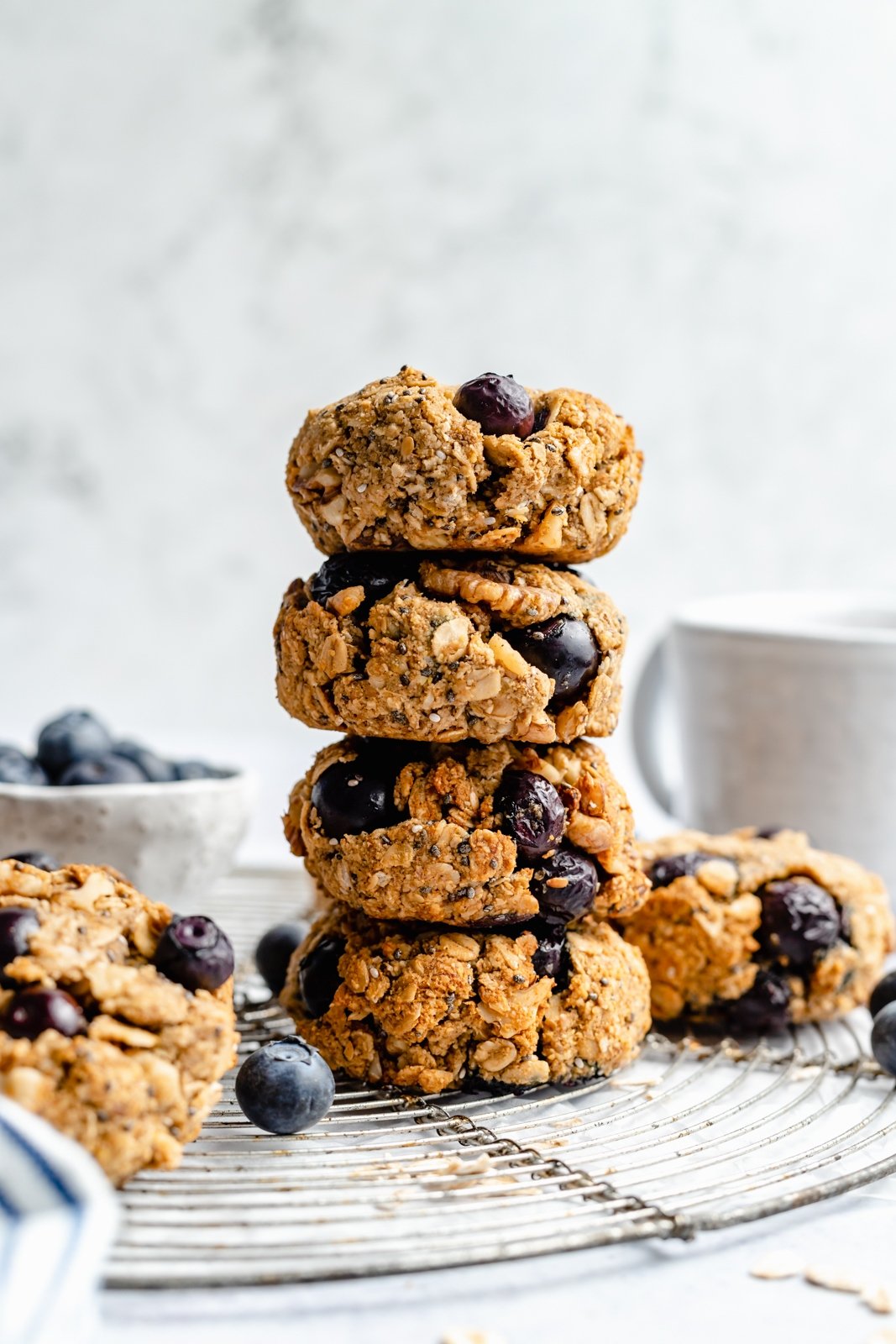 ¡Un tazón de galletas de desayuno de arándanos veganas y sin gluten que saben como muffins de arándanos! Estas saludables galletas de arándanos para el desayuno son naturalmente dulces y están llenas de nutrientes como semillas de chía, lino, avena, nueces y más. ¡Perfecto para congelar, es el desayuno o merienda perfecto para las semanas ocupadas! Una pila de galletas de desayuno de arándanos saludables