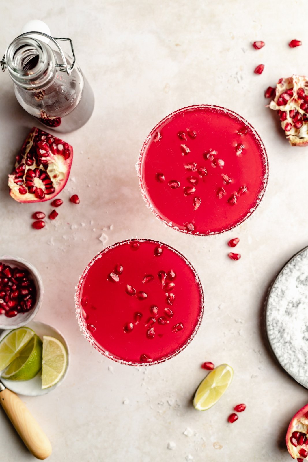 ¡Deliciosas y fáciles margaritas de granada hechas con cuatro ingredientes simples para el cóctel refrescante perfecto! Use jugo de granada comprado en la tienda o hecho en casa y jarabe simple para crear un maravilloso cóctel perfecto para el entretenimiento. Vista superior de dos margaritas de granada en copas
