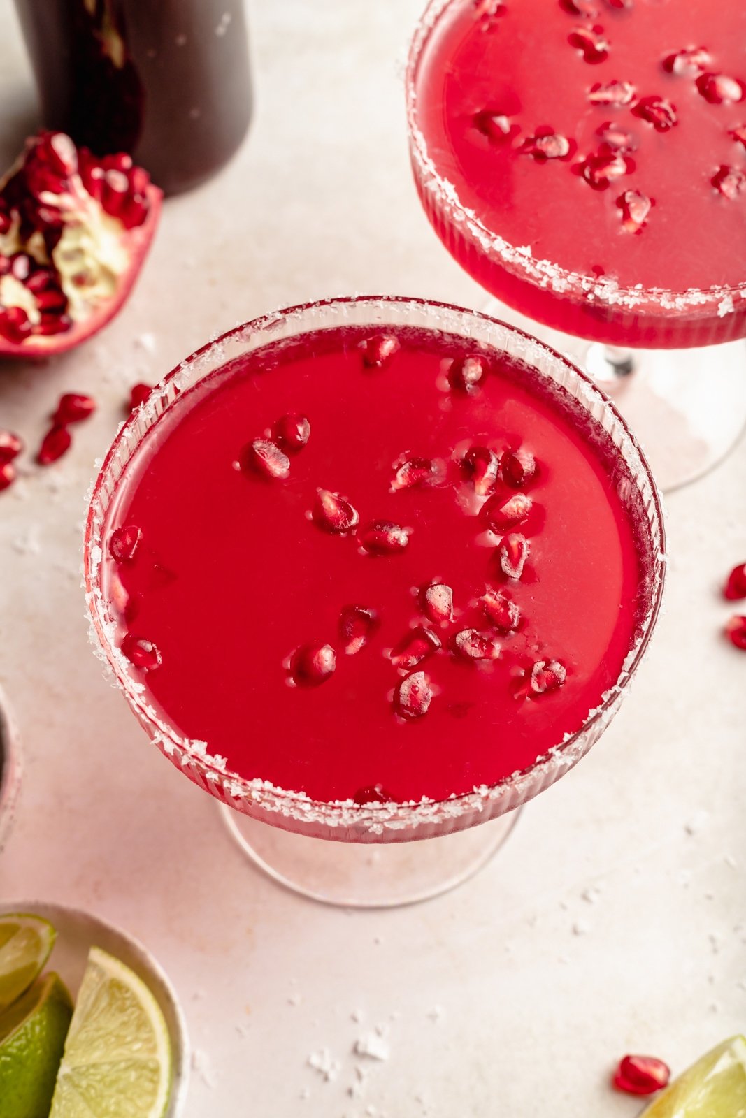 Una margarita de granada deliciosa y fácil hecha con cuatro ingredientes simples, ¡el cóctel refrescante perfecto! Use jugo de granada comprado en la tienda o hecho en casa y jarabe simple para crear un maravilloso cóctel perfecto para el entretenimiento. Dos margaritas de granada flacas con vasos