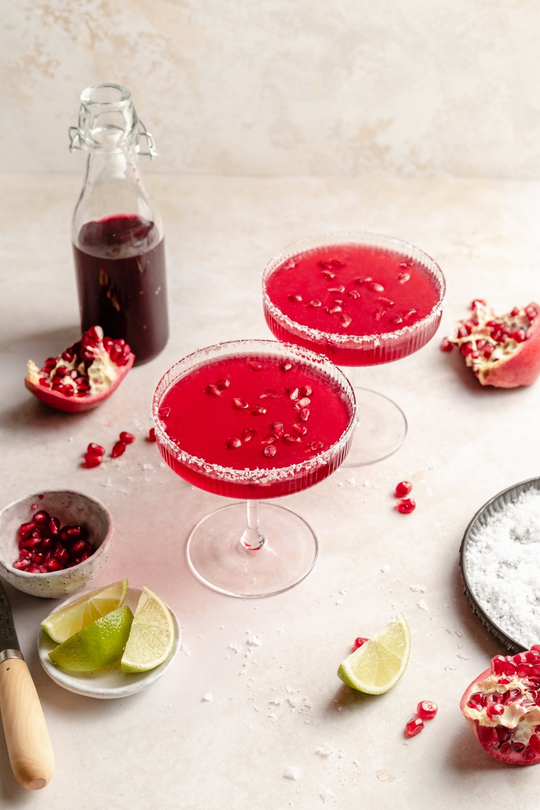 ¡Deliciosas y fáciles margaritas de granada hechas con cuatro ingredientes simples para el cóctel refrescante perfecto! Use jugo de granada comprado en la tienda o hecho en casa y jarabe simple para crear un maravilloso cóctel perfecto para el entretenimiento. Dos margaritas de granada con rodajas de lima y jugo de granada al lado