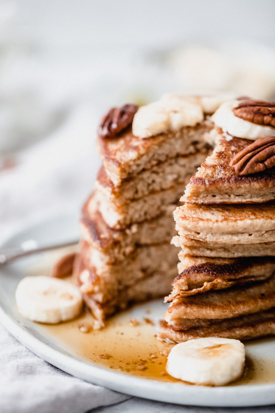 Panqueques de plátano y avena hechos directamente en la licuadora. Estos panqueques esponjosos y saludables son naturalmente libres de gluten, lácteos, harina y azúcar agregada. ¡Prepárate para un desayuno fácil y delicioso! Panqueques de plátano y avena apilados en un plato con un bocado