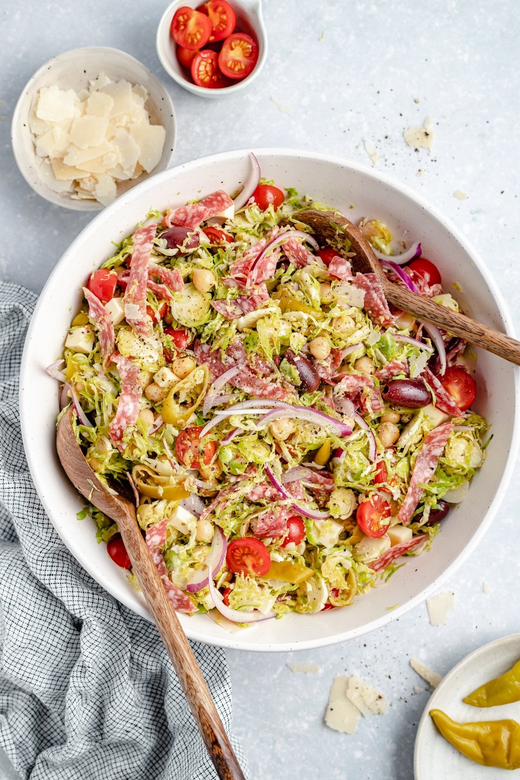 Magnífica receta de ensalada picada italiana con coles de Bruselas ralladas, garbanzos, verduras, salami, aceitunas, pepperoni y delicioso queso. ¡Esta deliciosa y fácil ensalada italiana de coles de Bruselas picadas con un ligero aderezo italiano es el almuerzo abundante perfecto o una cena fresca! Ensalada picada italiana fácil con coles de Bruselas en un tazón con pinzas de madera