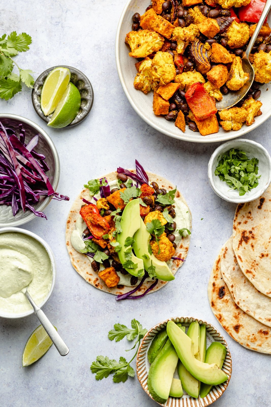 Hermosos tacos de vegetales asados rellenos con vegetales perfectamente sazonados y mucha proteína de origen vegetal. Sirve estos sencillos tacos veganos con aguacate, repollo rojo en rodajas, cilantro fresco y tu elección de dos salsas cremosas y deliciosas. ¡La mejor cena sin carne en una sola sartén! Tacos vegetarianos con verduras asadas y aguacate junto a un bol de verduras