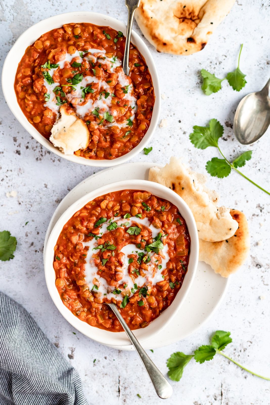 Sopa vegana nutritiva de lentejas con tomate y coco cocinada a fuego lento con deliciosas y cálidas especias como comino, cilantro y cúrcuma. ¡Esta receta cremosa de sopa de lentejas con tomate está repleta de proteínas de origen vegetal y es una preparación deliciosa para el almuerzo o la cena! Dos tazones de sopa vegana de tomate y lentejas con naan