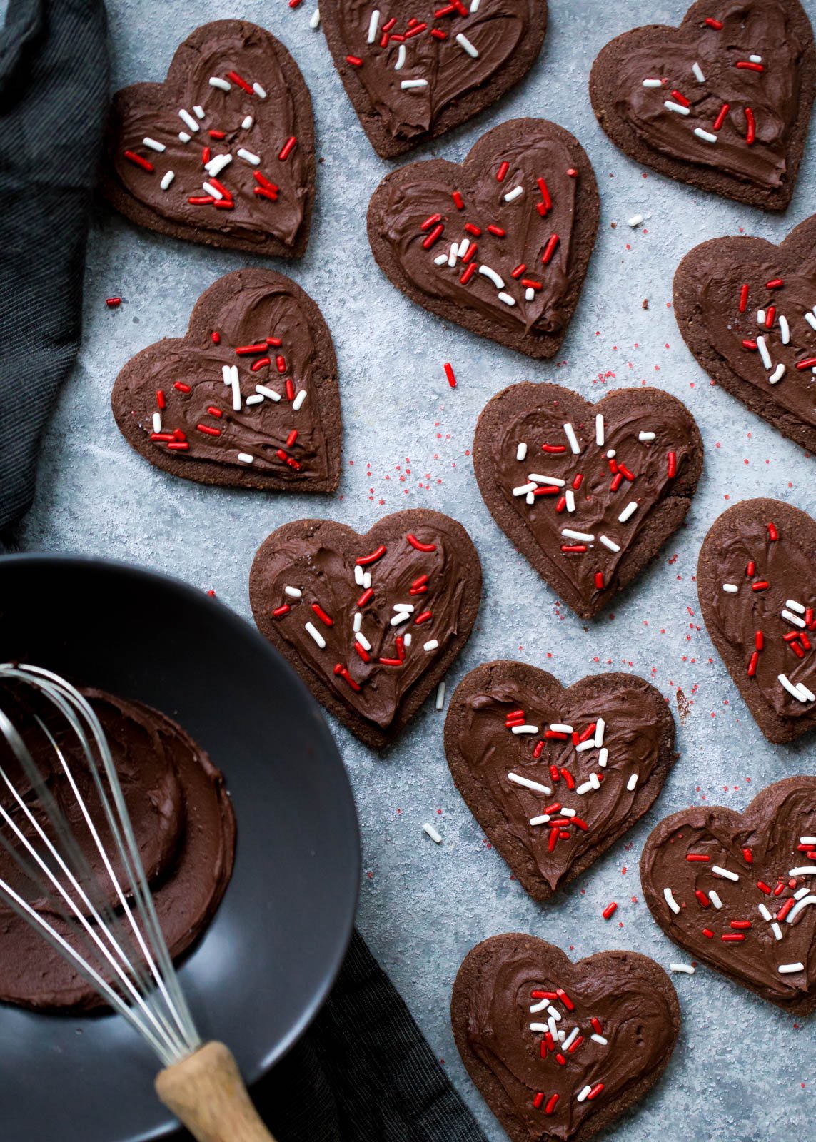 Deliciosas galletas de azúcar con chocolate y harina de almendras que no contienen cereales ni gluten. ¡Esta receta fácil de galletas de un tazón se puede cortar o enrollar en masa! Cubra con glaseado de chocolate sedoso y aterciopelado si lo desea. Galletas de azúcar de chocolate sin grano cortadas en forma de corazón junto a un tazón para mezclar