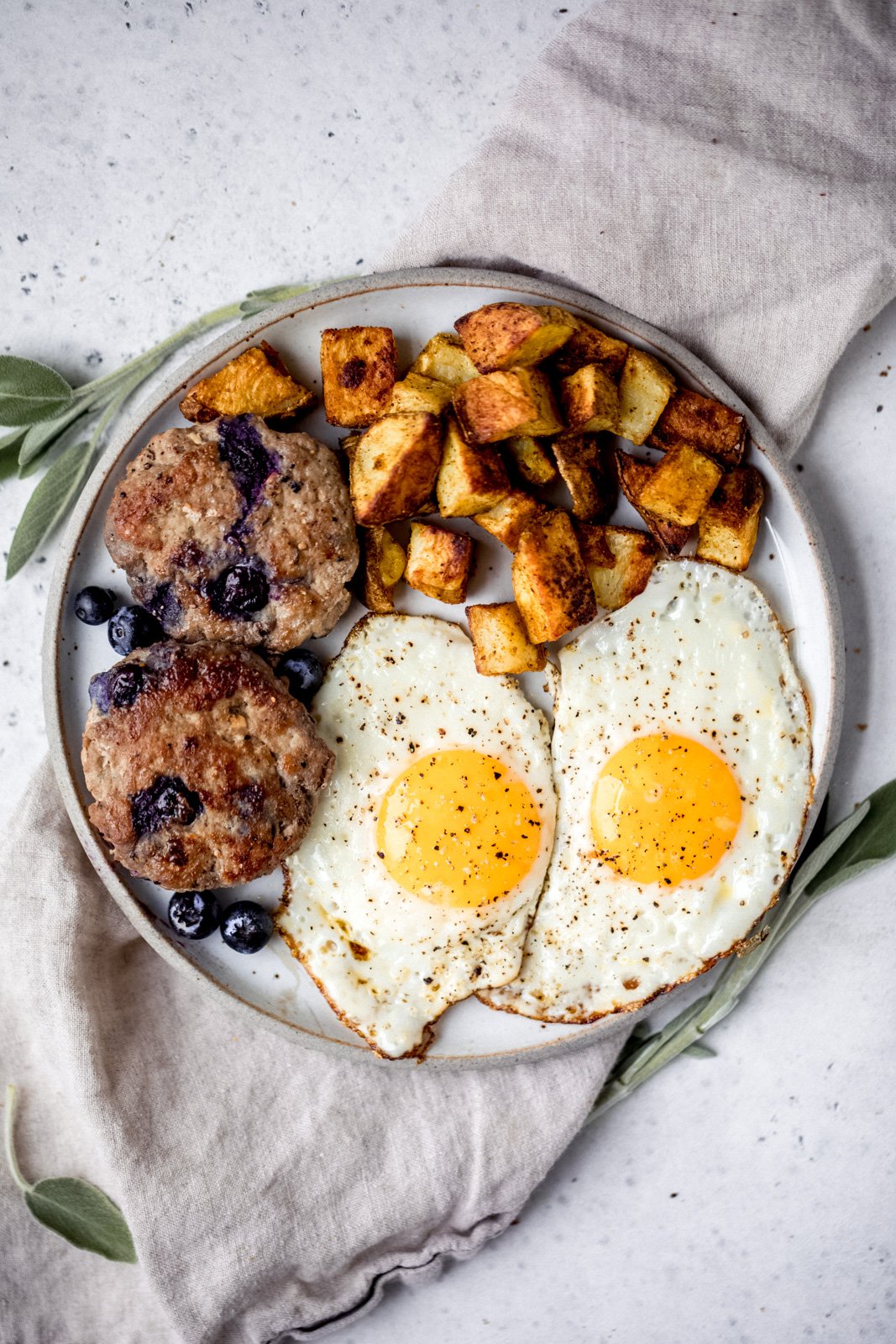 Dulces y deliciosos pays de desayuno de salchicha de pavo y arándanos Paleo Maple con deliciosas especias y jugosos arándanos en cada bocado. Sirve estas increíbles hamburguesas de salchicha de pavo con huevos fritos. ¡Disfruta del mejor desayuno rico en proteínas y bajo en carbohidratos! Pastel de salchicha de pavo y arándanos en un plato junto a papas y huevos para el desayuno