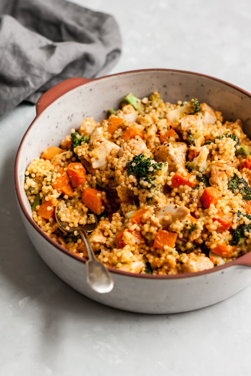 Cómodo y delicioso cuscús de pollo con queso cheddar y brócoli con calabaza asada dulce y picante. ¡Cualquier noche de la semana, te encantará esta receta fácil y reconfortante para la cena! Apto para niños y también fácil para vegetarianos. Cuscús de pollo con queso cheddar y brócoli en un tazón de cerámica con una cuchara