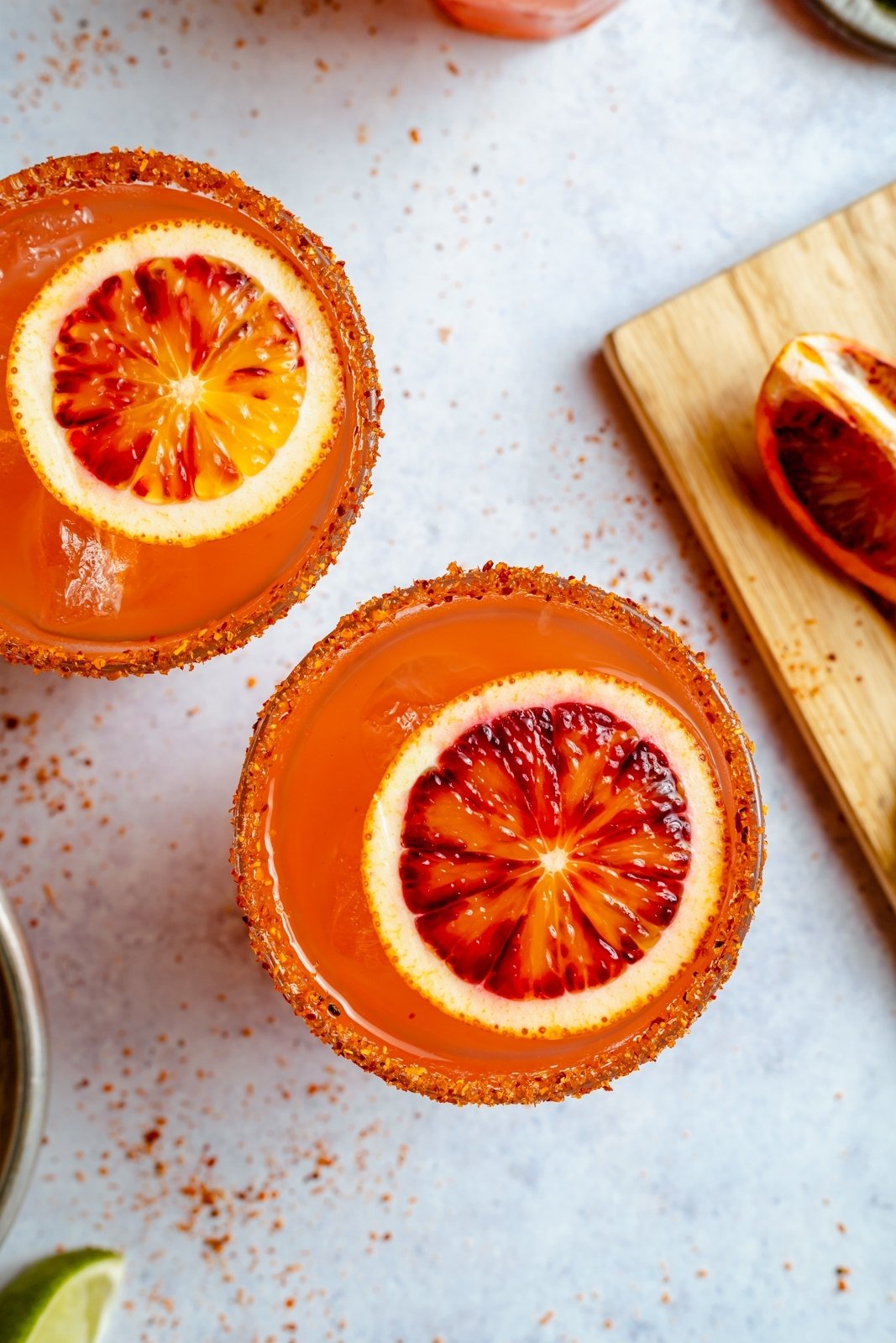 ¡Refrescante y deliciosa margarita picante de naranja sanguina hecha con 5 ingredientes simples! Esta hermosa receta de margarita de naranja sanguina es fácil de preparar y una forma divertida de disfrutar las naranjas sanguinas. ¡Perfecto para una cita nocturna, una noche de chicas o una cena triple para servir a la multitud! Vista superior de dos margaritas de naranja sanguina