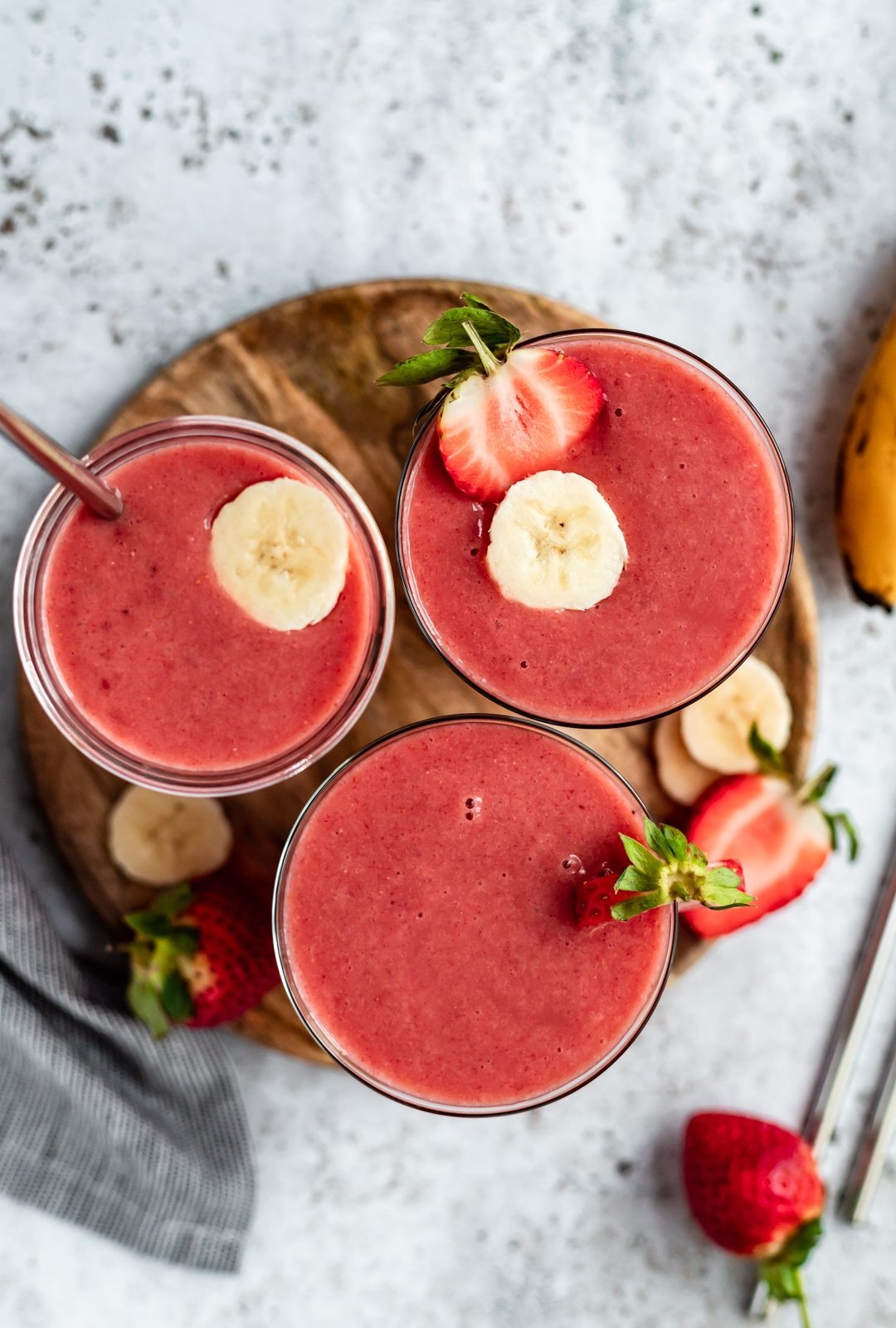 Recetas deliciosas y fáciles de plátano maduro para cada ocasión de merienda y postre. Encontrará recetas saludables con bananas, refrigerios indulgentes y formas únicas de usar bananas demasiado maduras en abundancia. ¡Incluye consejos para batidos, panes, panqueques, galletas e incluso plátanos congelados! Tres batidos de plátano naranja fresa en bandeja de madera