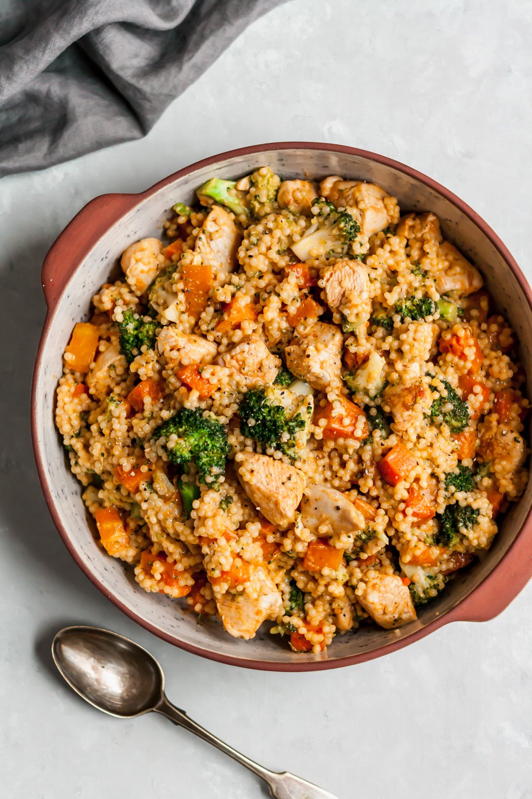 Reconfortante y delicioso cuscús de pollo con queso cheddar y brócoli mezclado con calabaza asada dulce y picante. ¡Te encantará esta receta de cena fácil y reconfortante cualquier noche de la semana! Es amigable para los niños y fácil ser vegetariano. Cuscús de pollo con queso cheddar y brócoli en una sartén junto a una cuchara