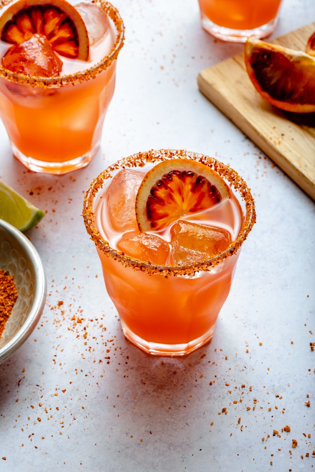 ¡Refrescante y deliciosa margarita picante de naranja sanguina hecha con 5 ingredientes fáciles! Esta hermosa receta de margarita de naranja sanguina es fácil de hacer y una forma divertida de disfrutar las naranjas sanguinas. ¡Perfecto para una cita nocturna, una noche de chicas o una cena triple sirviendo a una multitud! Dos vasos de margaritas de naranja sanguina sobre tabla de madera