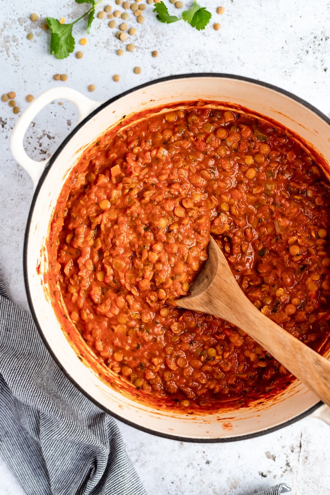 Nutritiva sopa vegana de lentejas, tomate y coco cocinada a fuego lento con deliciosas y cálidas especias como comino, cilantro y cúrcuma. ¡Esta receta de sopa cremosa de tomate y lentejas está cargada de proteínas de origen vegetal y es una deliciosa preparación para el almuerzo o la cena! Sopa vegana de tomate y lentejas en una olla con una cuchara de madera