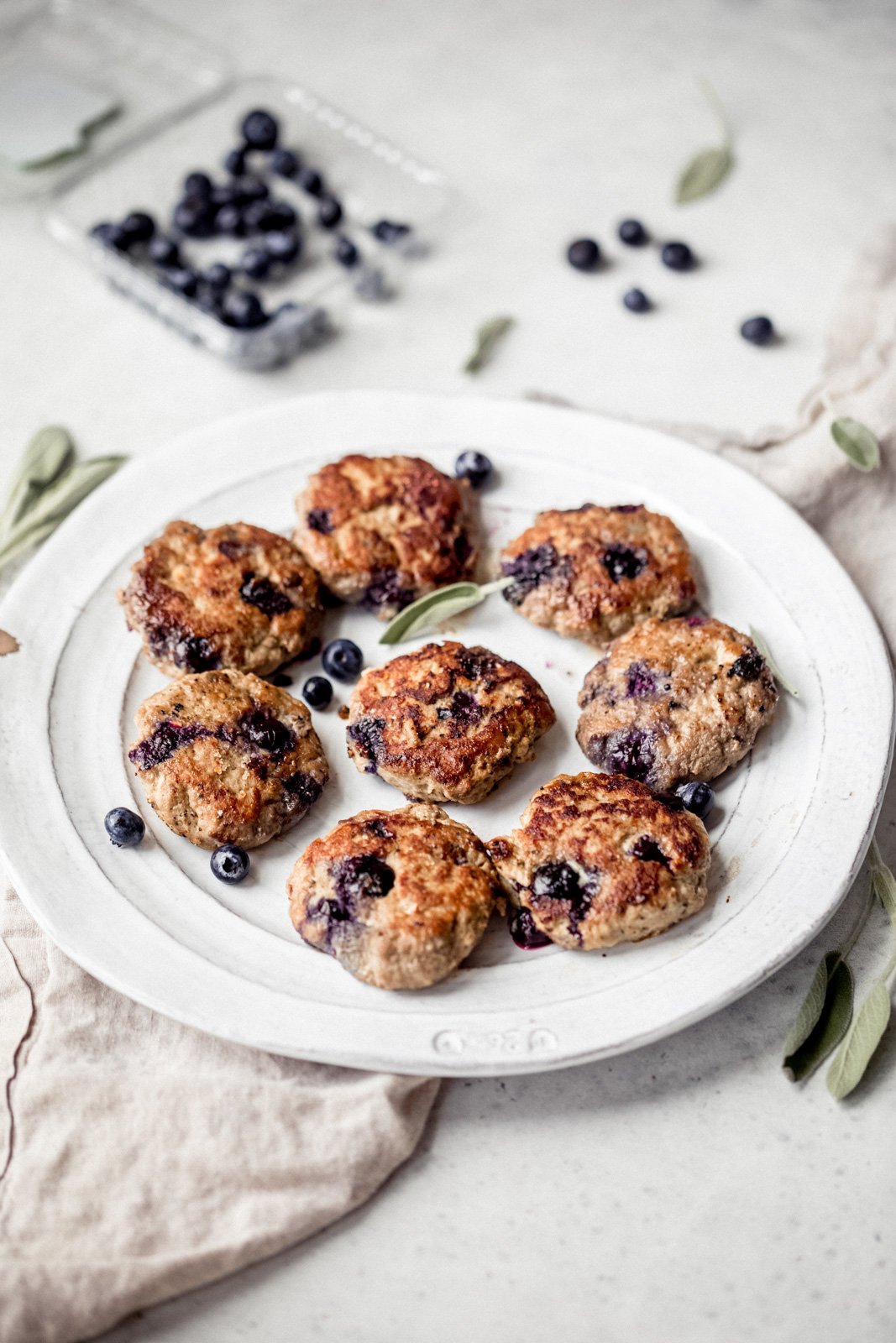 Dulce y salado Paleo Maple Blueberry Turkey Sausage Breakfast Pie con deliciosas especias y jugosos arándanos en cada bocado. ¡Sirve estas increíbles empanadas de salchicha de pavo con huevos fritos para obtener el mejor desayuno rico en proteínas y bajo en carbohidratos! Pastel de desayuno de salchicha de pavo en un plato con arándanos en el fondo