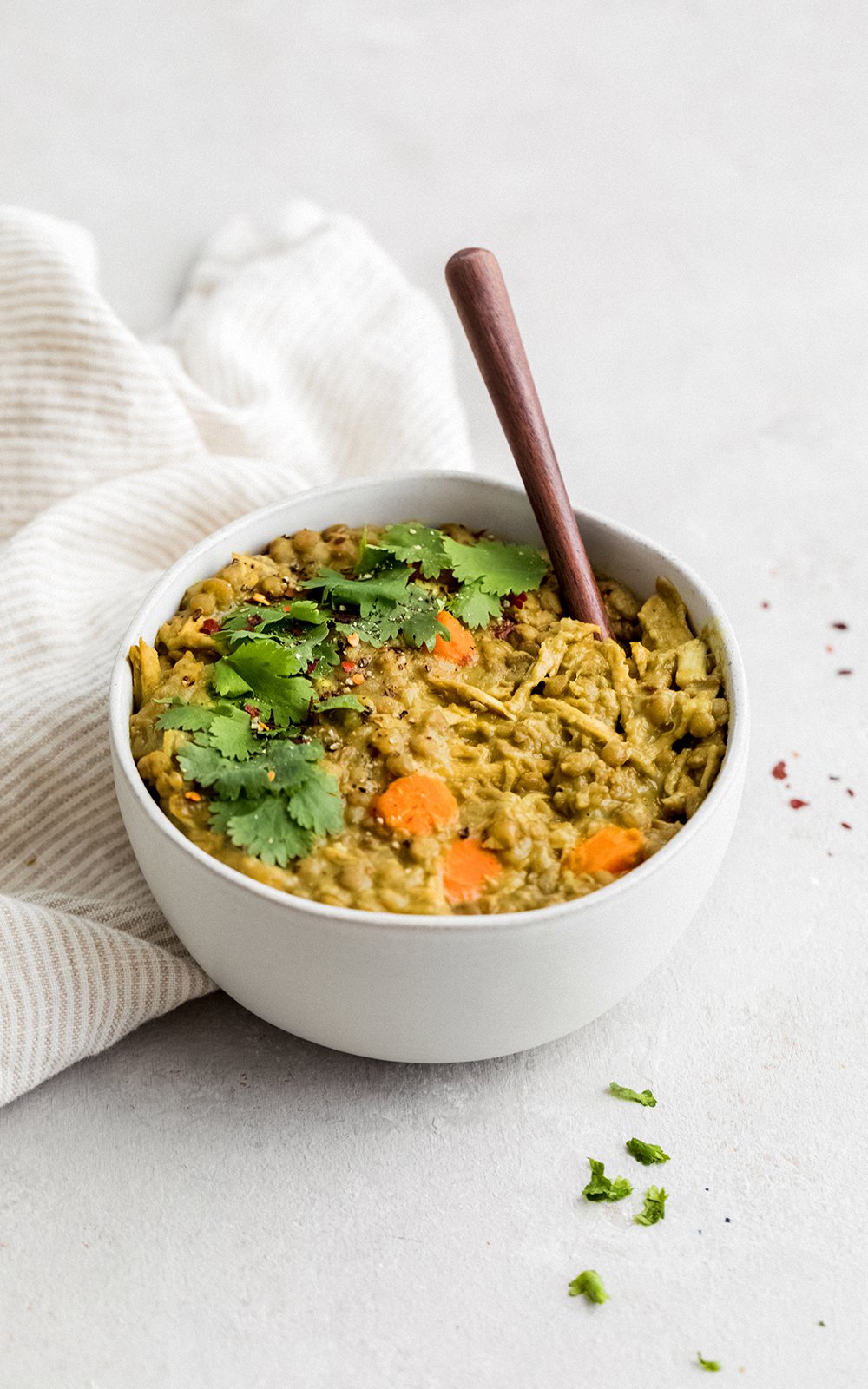 Deliciosa sopa de pollo y lentejas hecha con leche de coco cremosa y rellena con la bondad de la cúrcuma, el jengibre, el ajo y el comino. ¡Esta sopa cremosa de pollo y lentejas con coco dorado está repleta de proteínas y es el almuerzo o la cena perfectos y abundantes! Sopa cremosa de pollo y lentejas servida en un bol con una cuchara de madera