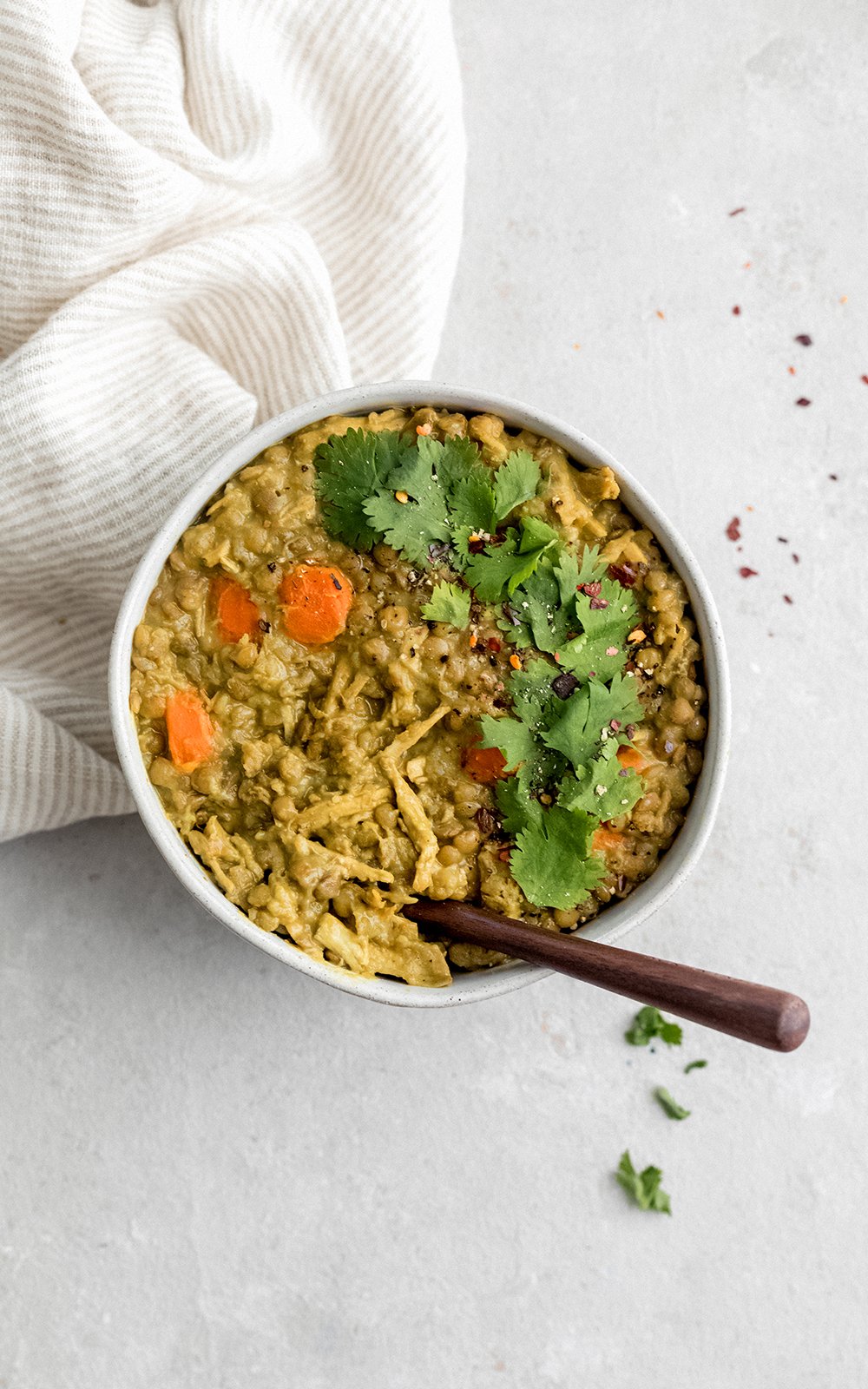 La maravillosa sopa de pollo y lentejas está hecha con leche de coco cremosa y está rellena con la bondad de la cúrcuma, el jengibre, el ajo y el comino. ¡Esta sopa cremosa de pollo y lentejas con coco dorado está repleta de proteínas y es el almuerzo o la cena perfectos y abundantes! Sopa de pollo con lentejas en un tazón con cuchara de madera
