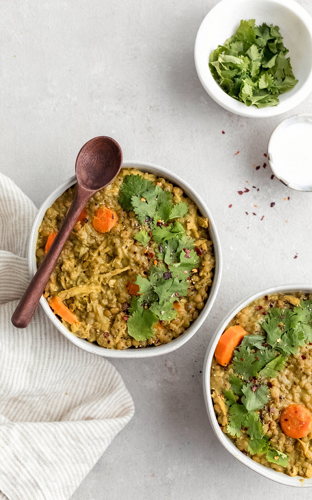 Sopa sabrosa de pollo y lentejas hecha con leche de coco cremosa y rellena con las bondades de la cúrcuma, el jengibre, el ajo y el comino. ¡Esta sopa cremosa de pollo y lentejas con coco dorado está repleta de proteínas y es el almuerzo o la cena perfectos y abundantes! Dos tazones de sopa de pollo y lentejas con una cuchara de madera