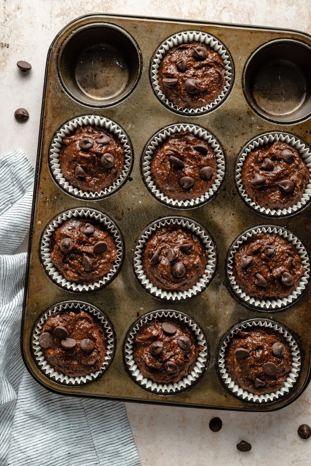 ¡Deliciosos muffins de plátano y chocolate con doble chocolate y tahini que saben a postre! Estos muffins de plátano y chocolate sin granos resultan ser Paleo, sin lácteos, sin gluten, endulzados de forma natural y perfectos para el desayuno o la merienda. Muffins de plátano y chocolate sin gluten sin hornear en una bandeja para hornear