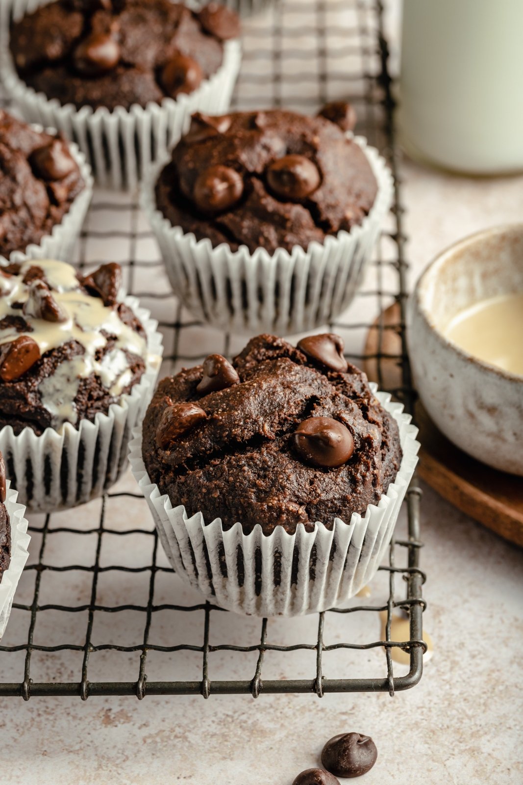 ¡Deliciosos muffins de plátano y chocolate con doble chocolate y tahini que saben a postre! Estos muffins de plátano y chocolate sin granos resultan ser Paleo, sin lácteos, sin gluten, endulzados de forma natural y perfectos para el desayuno o la merienda. Muffins de plátano y chocolate Paleo sobre una rejilla