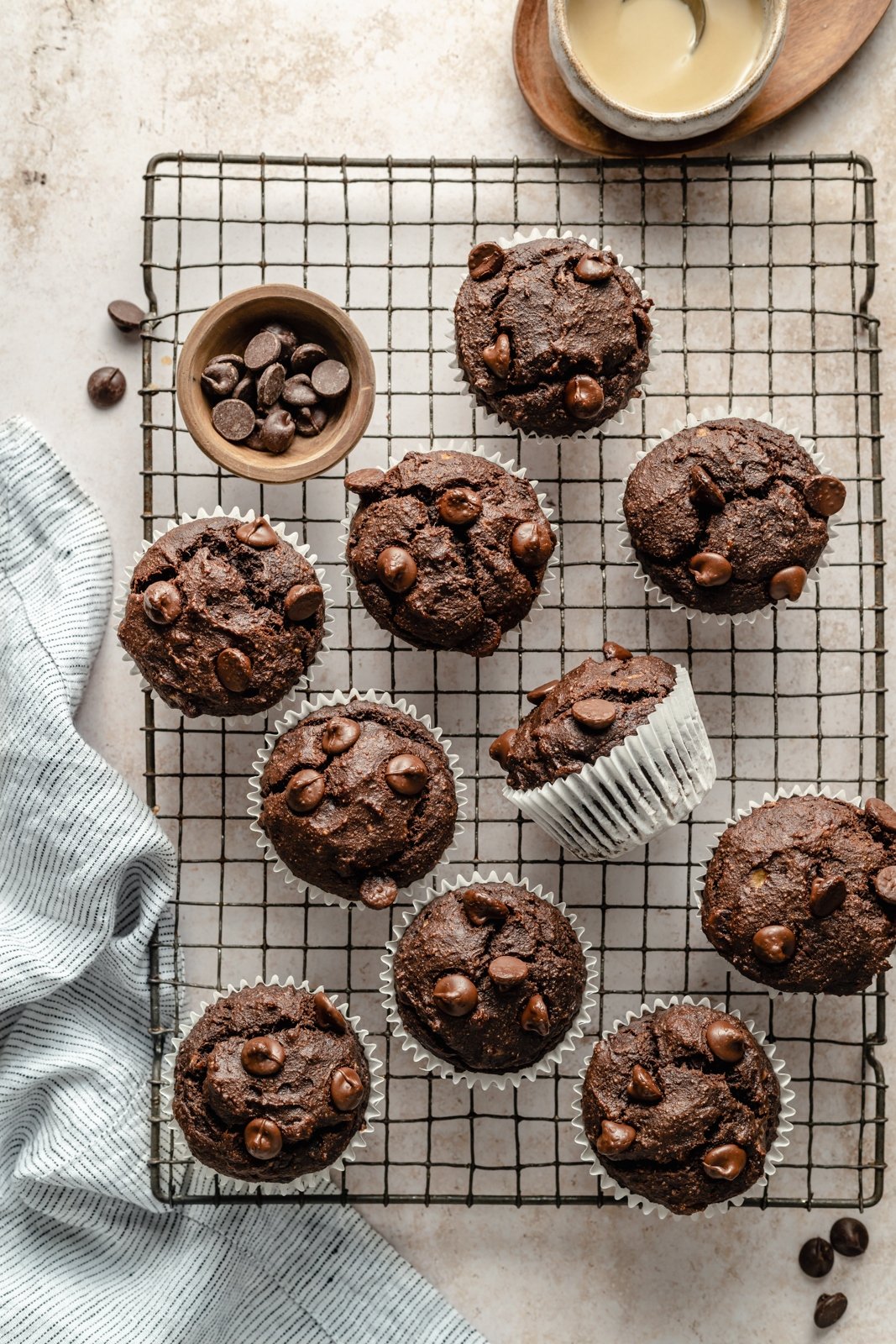 ¡Deliciosas magdalenas de banana con tahini y doble chocolate que saben a postre! Estos muffins de plátano y chocolate sin granos resultan ser paleo, sin lácteos, sin gluten y endulzados naturalmente, lo que los convierte en el desayuno o merienda perfecto. Muffins de Tahini y Plátano en una Rejilla de Alambre