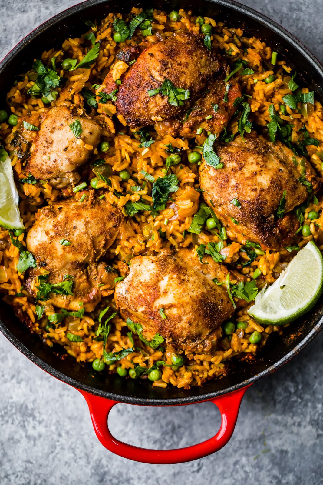 El famoso pollo y arroz puertorriqueño de mi mamá, también conocido como arroz con pollo, está hecho con sofrito de pollo sazonado con adobo casero y arroz sabroso en una sola sartén. Es un plato reconfortante, fácil de preparar y la comida nutritiva perfecta entre semana. ¡Haré esta receta una y otra vez! arroz con pollo en una sartén adornado con cilantro y lima
