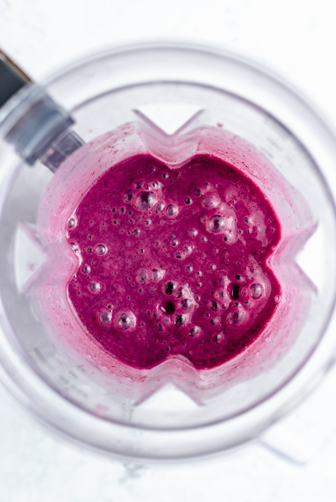 Magnífico batido de limón y arándanos hecho con jugo de limón fresco y jugosos arándanos para una explosión de sabor. Este sencillo batido vegano de limón y arándanos está endulzado naturalmente con fruta y hecho con solo cinco ingredientes simples. Opción de agregar su fortificante nutricional favorito para el perfecto desayuno o merienda! Vista de arriba hacia abajo del batido de arándanos y limón en la licuadora