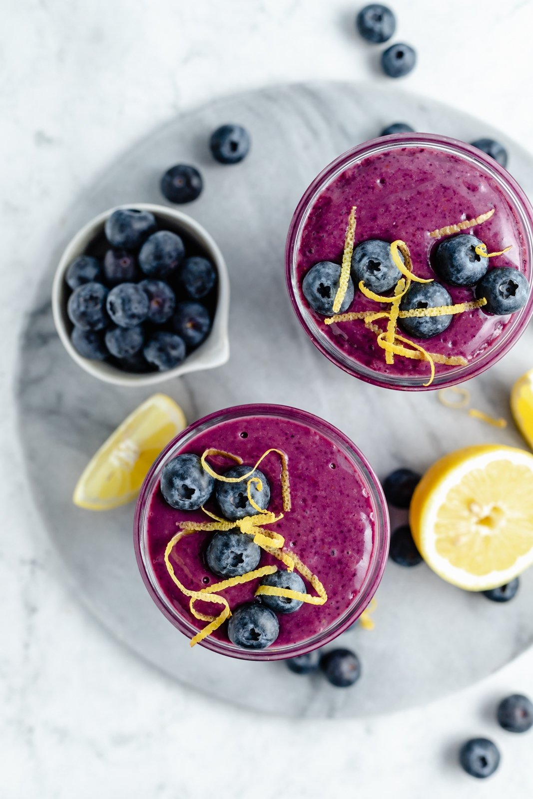 Magnífico batido de limón y arándanos hecho con jugo de limón fresco y jugosos arándanos para una explosión de sabor. Este sencillo batido vegano de limón y arándanos está endulzado naturalmente con fruta y hecho con solo cinco ingredientes simples. Opción de agregar su refuerzo nutricional favorito para el perfecto #smoothie #blueberries #breakfast #vegan #dairyfree #glutenfree #healthysnack #healthybreakfast Magnífico batido de limón y arándanos con jugo de limón fresco y jugosidad El brillante sabor de los arándanos. Este sencillo batido vegano de limón y arándanos está endulzado naturalmente con fruta y solo cinco ¡Opciones sencillas para agregar su potenciador nutricional favorito al desayuno o merienda perfecto! Vista superior de dos batidos de limón y arándanos