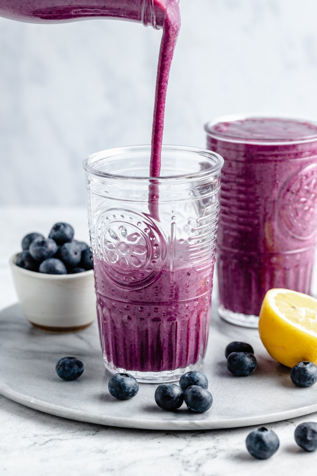 Un delicioso batido de limón y arándanos con sabores brillantes de jugo de limón fresco y jugosos arándanos. Este sencillo batido vegano de limón y arándanos se endulza de forma natural con fruta y se prepara con solo cinco ingredientes simples. ¡Opción de agregar su refuerzo nutricional favorito para el desayuno o merienda perfecto! Vierta el batido de arándanos y limón en un vaso