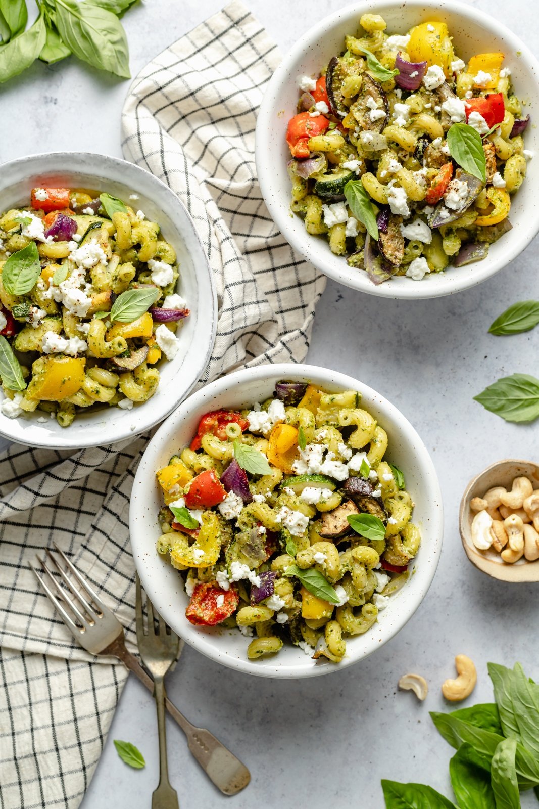 Pasta brillante y deliciosa con verduras asadas servida con un delicioso pesto casero de marañón y queso cremoso de cabra. Esta receta fácil de pasta de vegetales asados presenta vegetales frescos y coloridos que se pueden servir fríos o calientes como ensalada de pasta. ¡Opción para asar verduras y agregar tu proteína favorita! Tres tazones de pasta fácil de vegetales asados