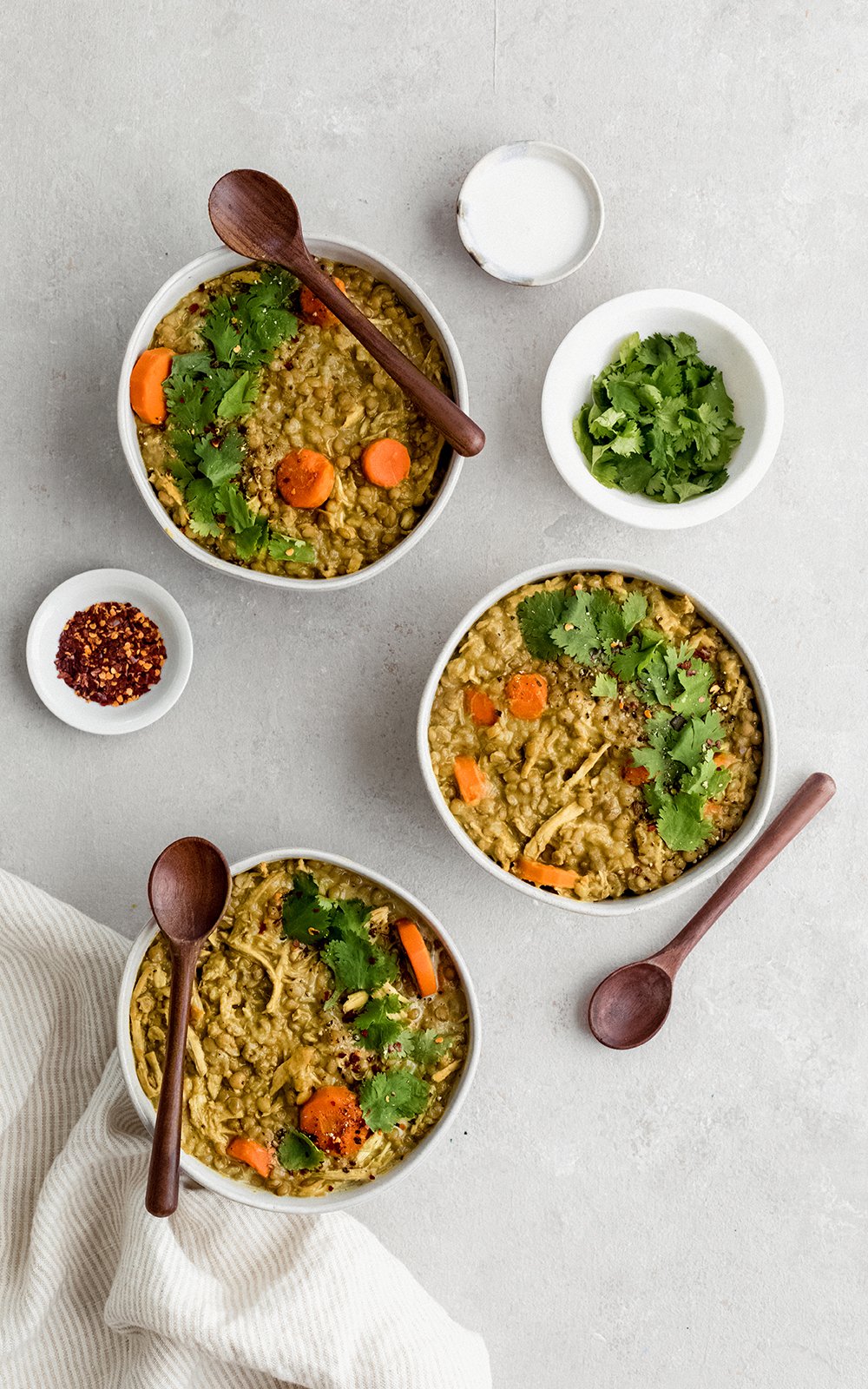 Deliciosa sopa de pollo y lentejas hecha con leche de coco cremosa y rellena con la bondad de la cúrcuma, el jengibre, el ajo y el comino. ¡Esta sopa cremosa de pollo y lentejas con coco dorado está repleta de proteínas y es el almuerzo o la cena perfectos y abundantes! Tres tazones de sopa de pollo y lentejas con cuchara de madera