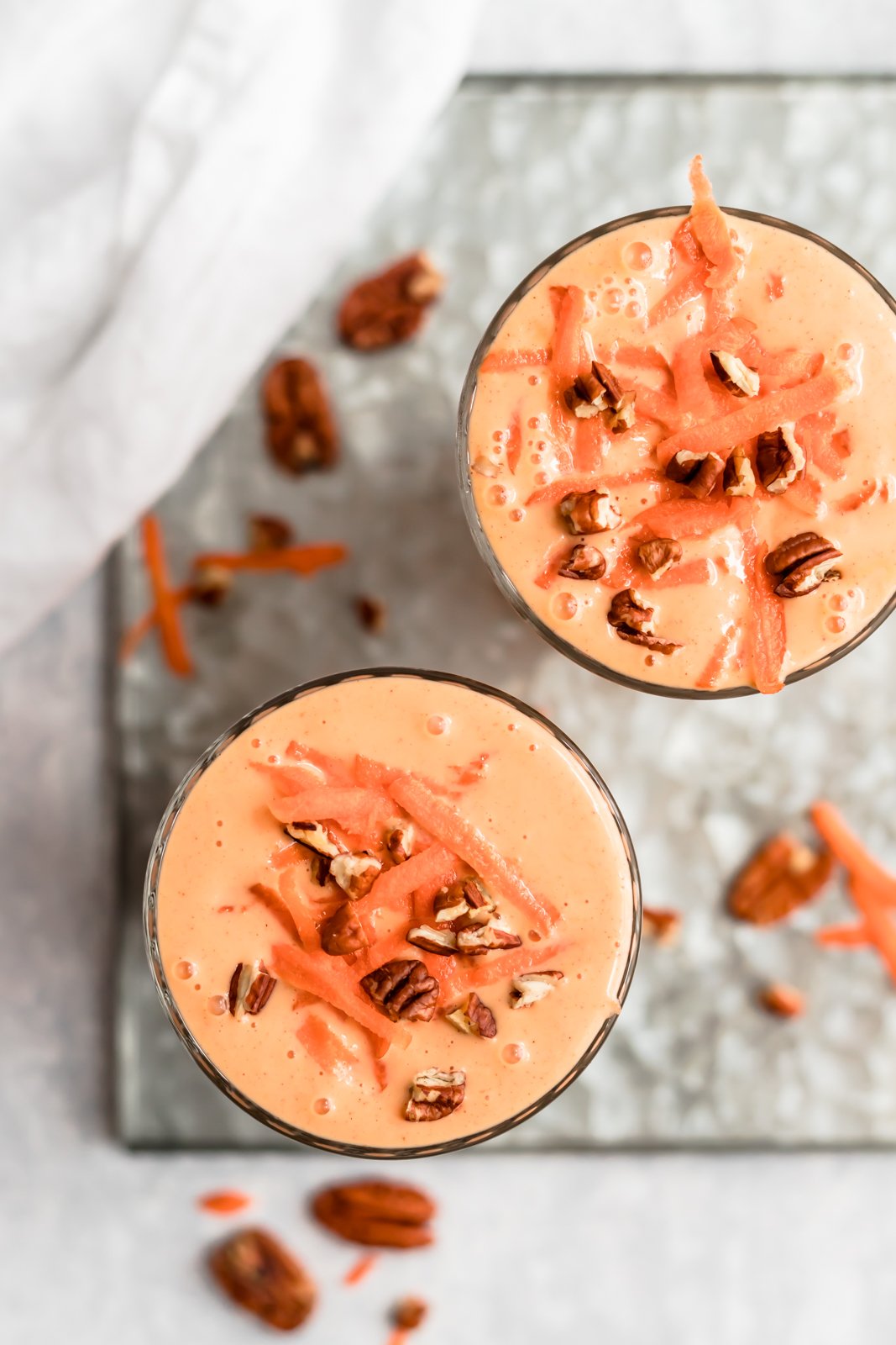 Licuado de pastel de zanahoria sabroso y saludable hecho con ingredientes saludables como zanahorias crudas, plátanos, piña, leche de coco cremosa, yogur griego y muchas especias reconfortantes. Este batido de pastel de zanahoria repleto de proteínas es perfecto para el desayuno o después del entrenamiento ¡merienda! Dos batidos de pastel de zanahoria cubiertos con zanahorias ralladas y nueces
