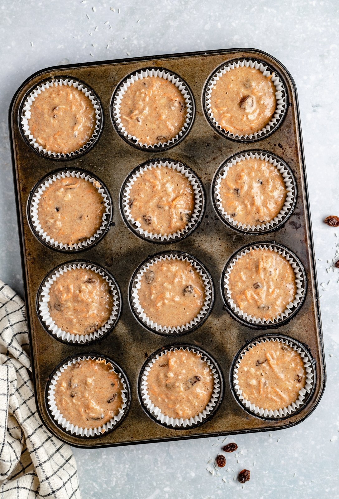 Muffins de pastel de zanahoria saludables rellenos de zanahorias, coco, pasas y nueces. Estos muffins de pastel de zanahoria deliciosamente húmedos están endulzados de forma natural con jarabe de arce puro y compota de manzana. Cubiertos con un glaseado de queso crema ligero, sirva como un refrigerio delicioso o como un saludable ¡merienda! Muffins saludables de pastel de zanahoria sin hornear en moldes para muffins
