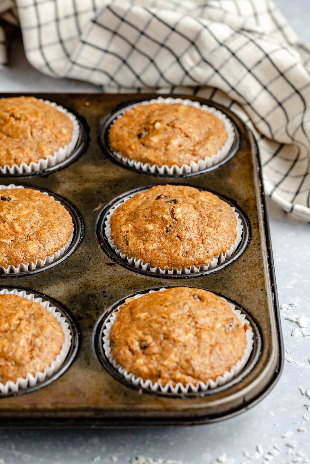 Muffins de pastel de zanahoria saludables rellenos de zanahorias, coco, pasas y nueces. Estos muffins de pastel de zanahoria deliciosamente húmedos están endulzados naturalmente con jarabe de arce puro y compota de manzana. ¡Cubra con un glaseado de queso crema ligero para un refrigerio delicioso o una golosina saludable! Muffins de pastel de zanahoria saludables en moldes para muffins