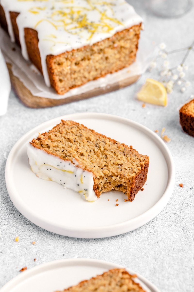 Increíble pan saludable de semillas de amapola y limón hecho de una mezcla de harina de avena y almendras y endulzado naturalmente con miel. ¡Este pan fácil de semillas de amapola y limón sin gluten está repleto de proteínas de yogur griego y es un desayuno o merienda fácil y saludable en un tazón! Una rebanada de pan de semilla de amapola de limón saludable en un plato