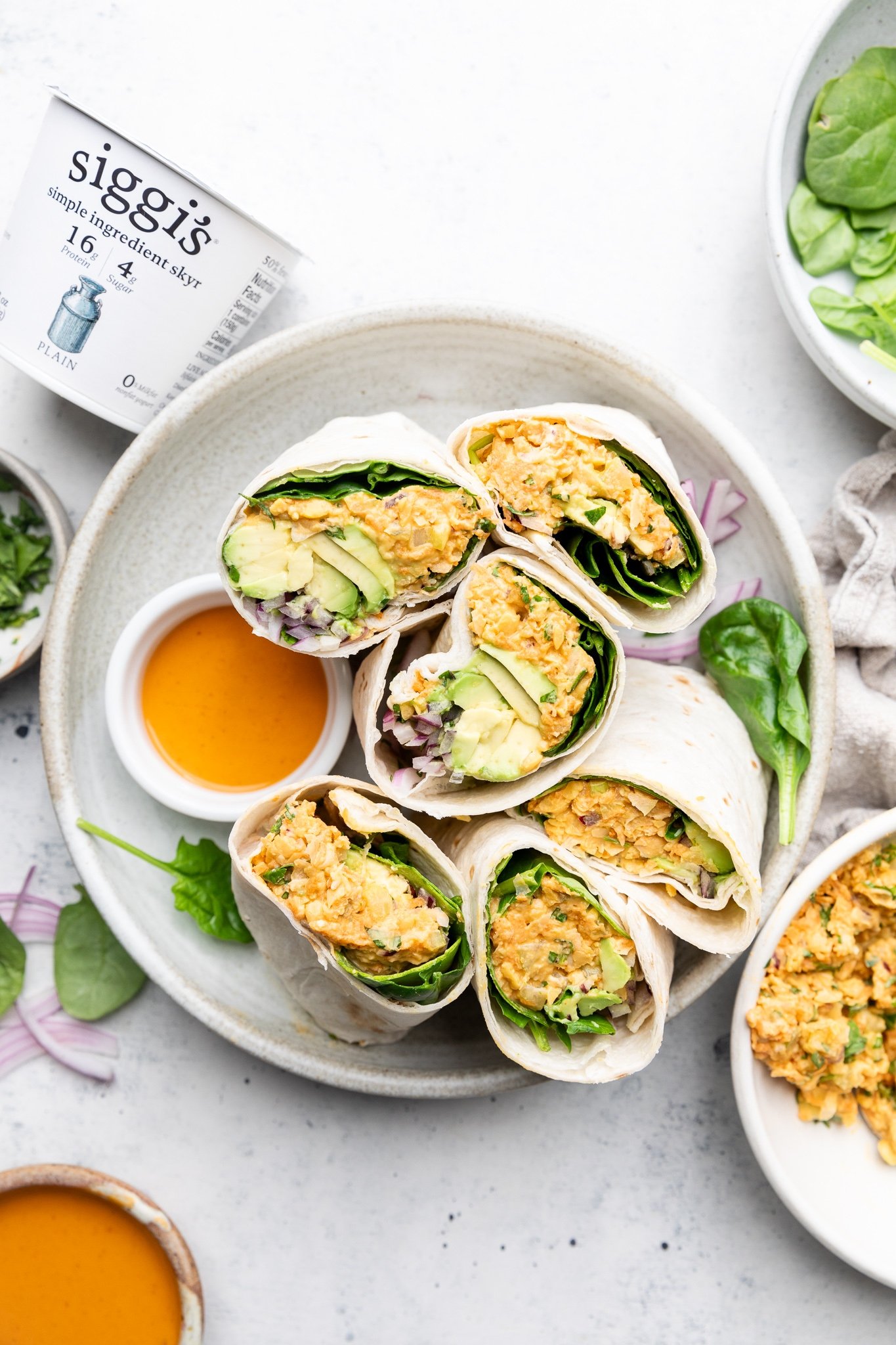 Una deliciosa ensalada de garbanzos buffalo envuelve verduras crujientes, aguacate cremoso y espinacas frescas. ¡Gracias al yogur de siggi y una lata entera de garbanzos, estas fáciles envolturas de garbanzos de búfalo están llenas de proteínas y son el almuerzo perfecto para los días de semana! Ensalada De Garbanzos Búfalo Rebanados Envueltos En Un Plato