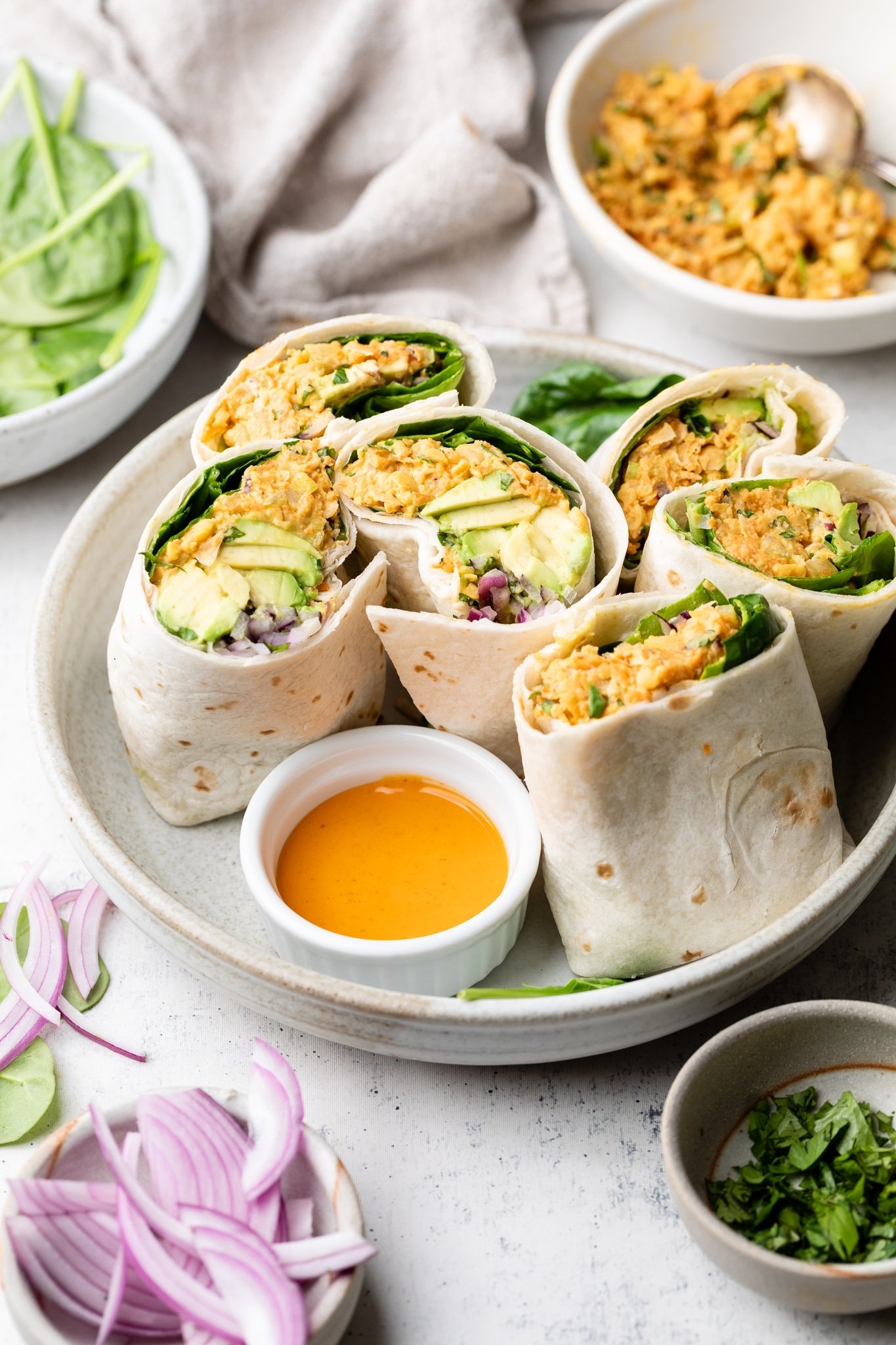 Sabrosos wraps de ensalada de garbanzos estilo buffalo con verduras crujientes, aguacate cremoso y espinacas frescas. Gracias al yogur siggi's y una lata entera de garbanzos, estos sencillos wraps de garbanzos buffalo están repletos de proteínas y son perfectos para los almuerzos empacables entre semana. Envolturas saludables de ensalada de garbanzos Buffalo a la mitad en un plato
