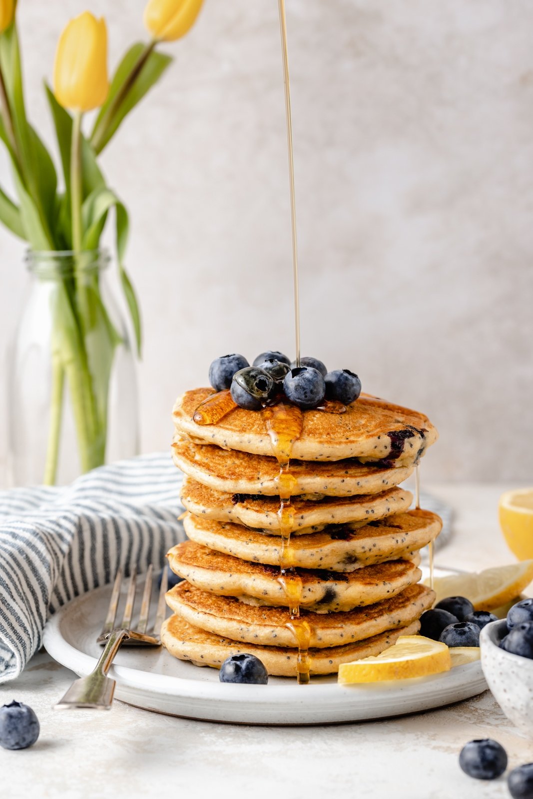 ¡Deliciosos panqueques esponjosos de limón y arándanos con yogur griego para un gran refuerzo de proteínas! Hechos con harina de avena, estos panqueques saludables de limón y arándanos no contienen gluten y están repletos de los sabores brillantes de los arándanos frescos, el jugo de limón y la ralladura. ¡Agregue semillas de amapola para un ambiente primaveral encantador, y no olvide cubrir con bayas adicionales! Rocíe jarabe en una pila de panqueques de limón y arándanos sin gluten