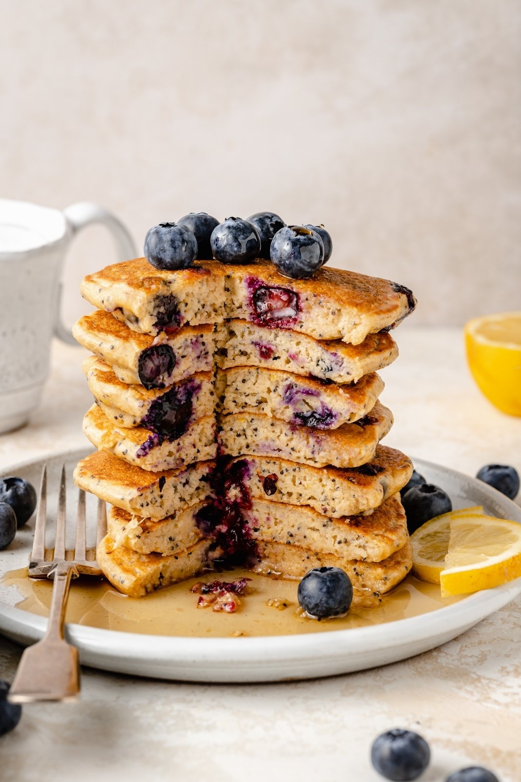 ¡Deliciosos panqueques esponjosos de limón y arándanos con yogur griego para un gran refuerzo de proteínas! Hechos con harina de avena, estos panqueques saludables de limón y arándanos no contienen gluten y están repletos de los sabores brillantes de los arándanos frescos, el jugo de limón y la ralladura. ¡Agregue semillas de amapola para un ambiente primaveral encantador, y no olvide cubrir con bayas adicionales! Pila de tortitas de limón y arándanos en un plato