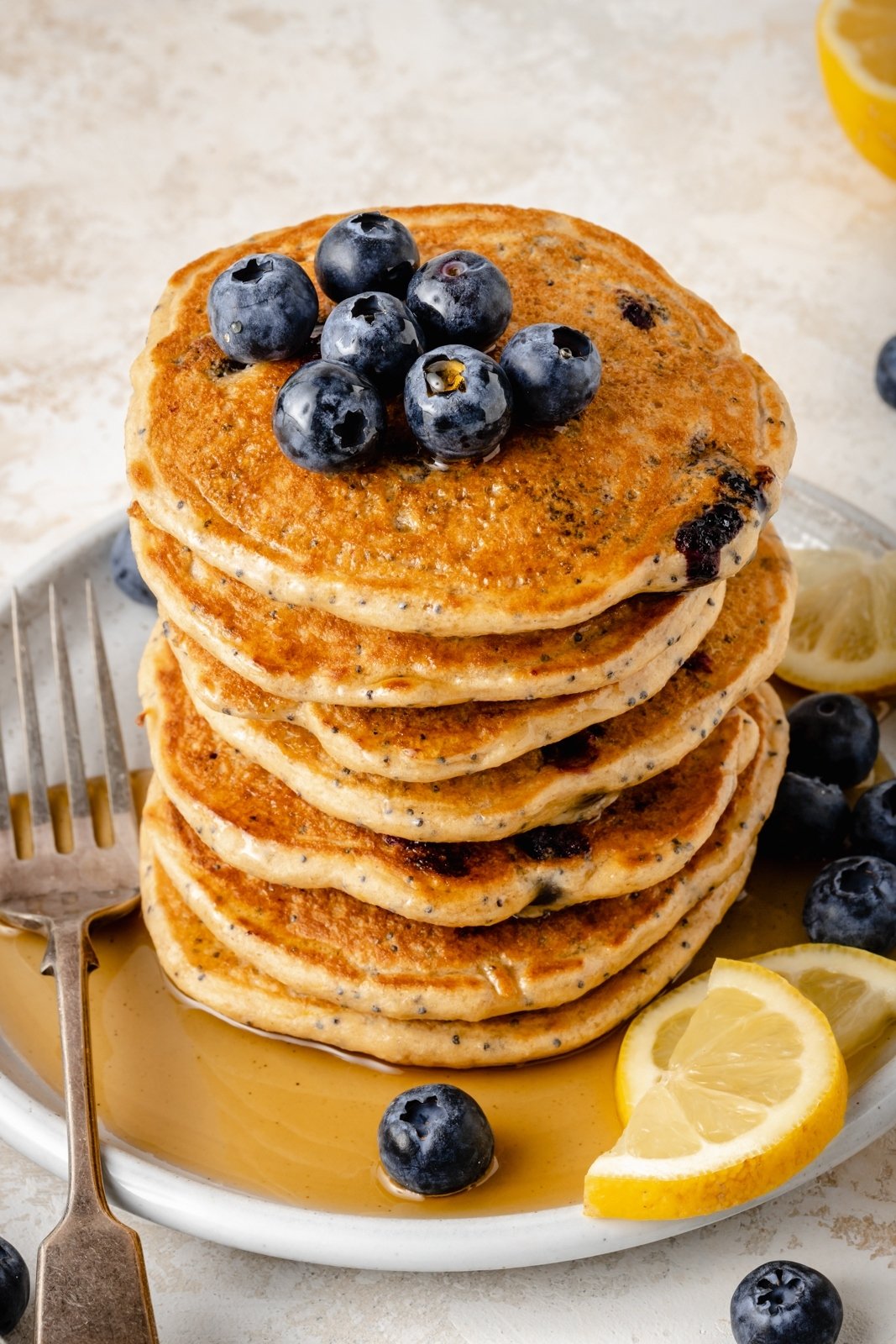 ¡Deliciosos y esponjosos Panqueques de Limón y Arándanos con Yogur Griego para un refuerzo de proteínas! Hechos con harina de avena, estos saludables Panqueques de Limón y Arándanos no contienen gluten y están rellenos con los sabores brillantes de arándanos frescos, jugo de limón y ralladura. Agregue semillas de amapola para ¡un encantador toque primaveral y no olvides las bayas adicionales en la parte superior! Montón de tortitas de limón y arándanos con yogur griego en un plato