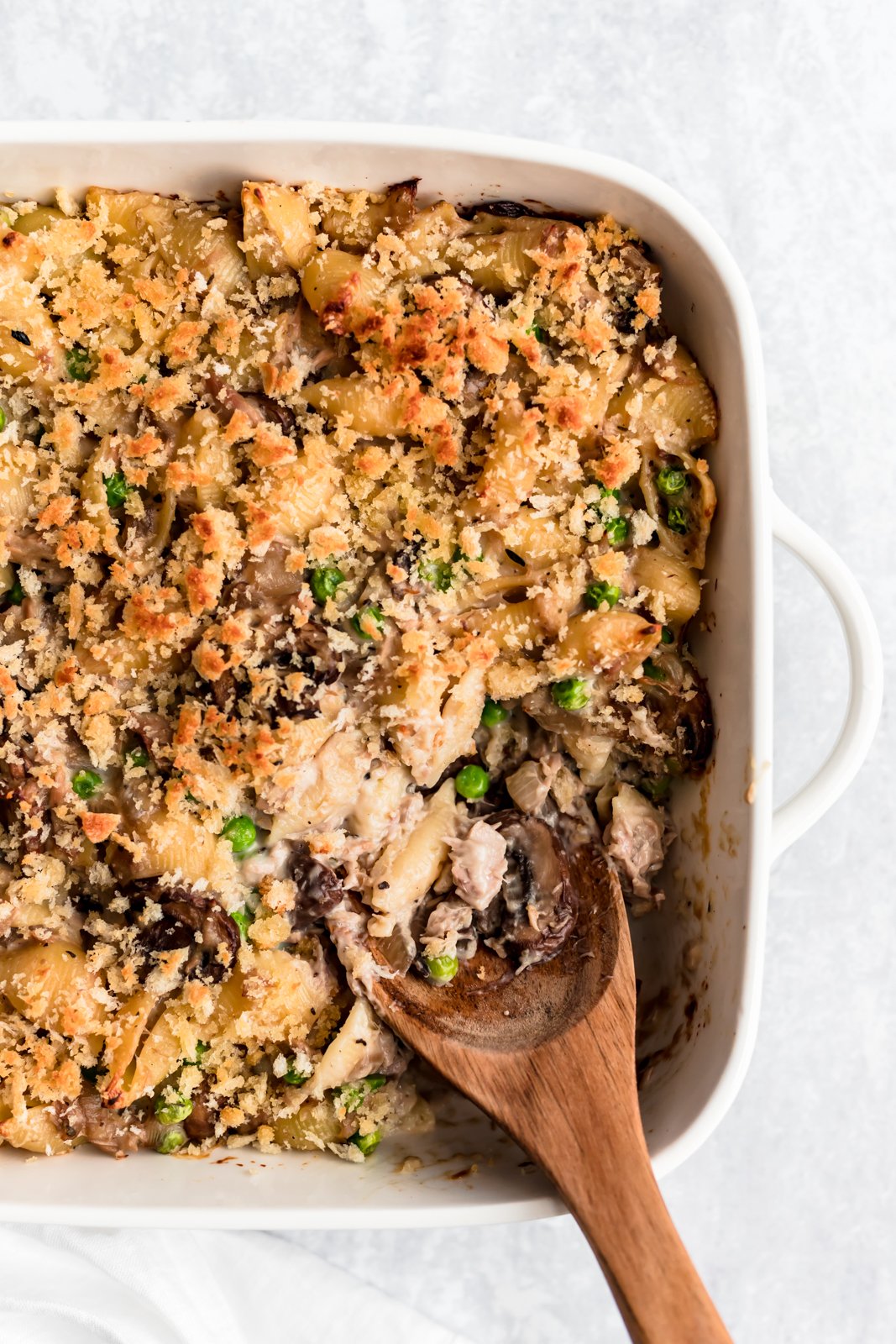 Si está buscando una cazuela de fideos de atún saludable hecha desde cero, ¡no busque más! ¡Esta cazuela de fideos de atún ligera está hecha con una salsa de champiñones parmesano cremosa pero ligera, fideos, atún enlatado y guisantes! ¡Enamórese de esta receta fácil para la cena, ¡seguramente se convertirá en un favorito para siempre! Cazuela de fideos de atún saludable en una sartén con una cuchara de madera