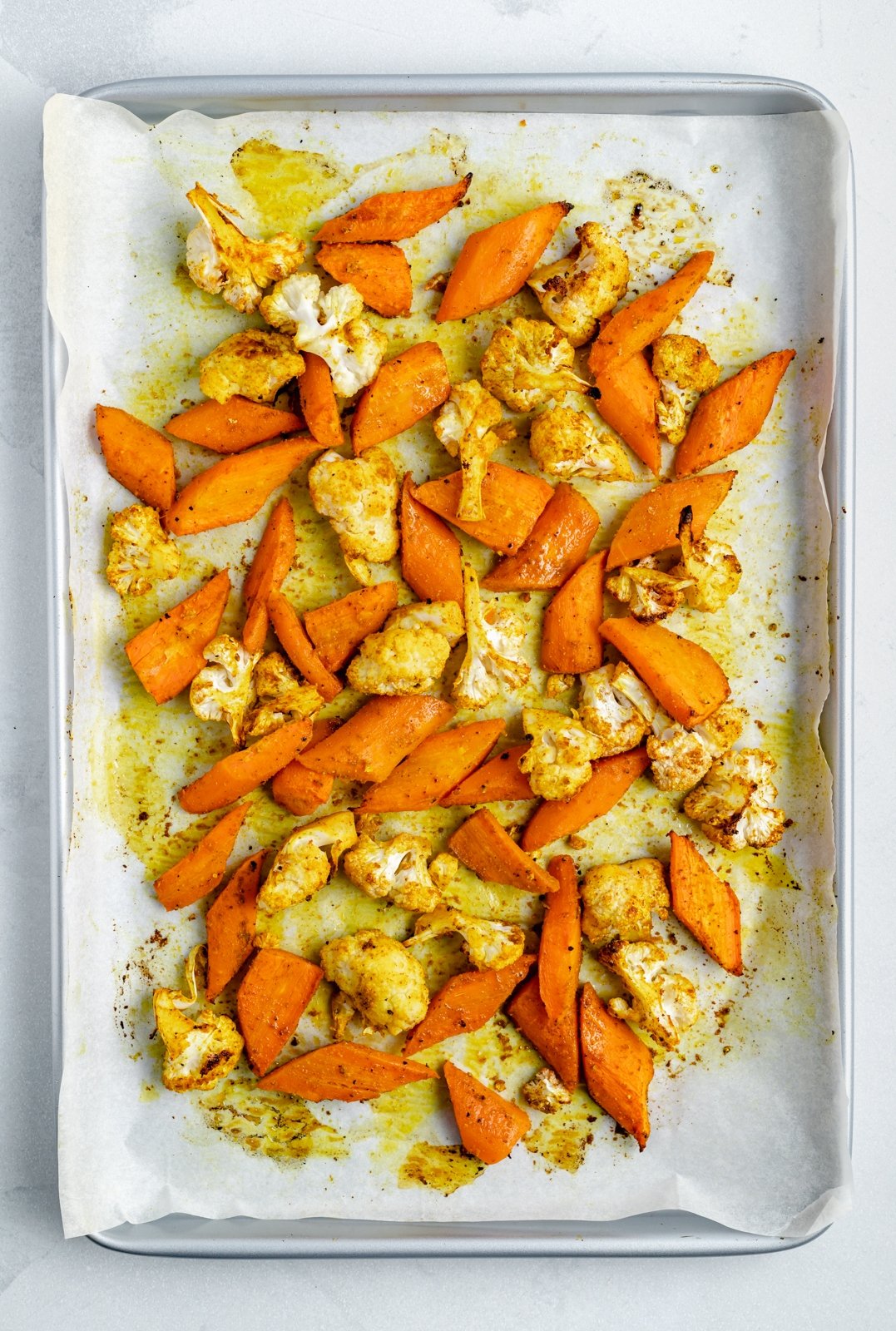 Hermosa ensalada de quinua, coliflor y zanahoria asada con hierbas frescas, deliciosos dátiles y pistachos salados. ¡Esta ensalada vegana de coliflor y quinua con aderezo soleado es el almuerzo o guarnición a base de plantas perfecta! Zanahorias asadas y coliflor en una bandeja para hornear