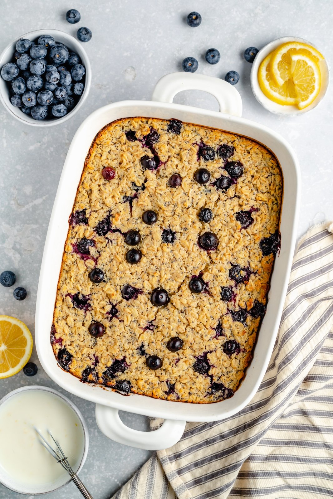 La hermosa avena horneada con limón y arándanos está hecha con jugo de limón fresco y ralladura de limón y endulzada naturalmente con jarabe de arce puro. Esta avena horneada con limón no contiene gluten ni lácteos y está repleta de arándanos frescos y semillas de amapola en cada bocado. ¡Rocíe con yogur de limón casero para el desayuno perfecto! Avena horneada con arándanos en una bandeja para hornear