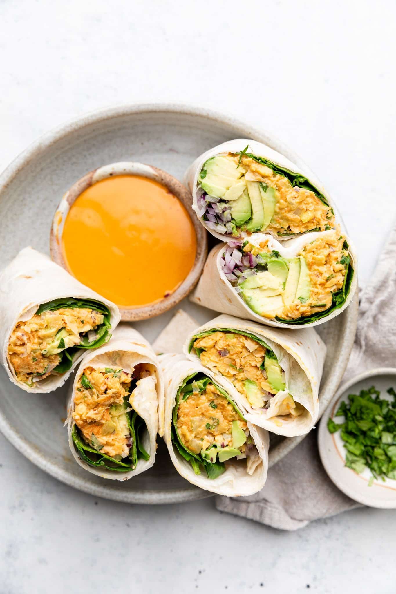 Una deliciosa ensalada de garbanzos buffalo envuelve verduras crujientes, aguacate cremoso y espinacas frescas. ¡Gracias al yogur de siggi y una lata entera de garbanzos, estas fáciles envolturas de garbanzos de búfalo están llenas de proteínas y son el almuerzo perfecto para los días de semana! Envolturas saludables de ensalada de garbanzos Buffalo, cortadas en platos