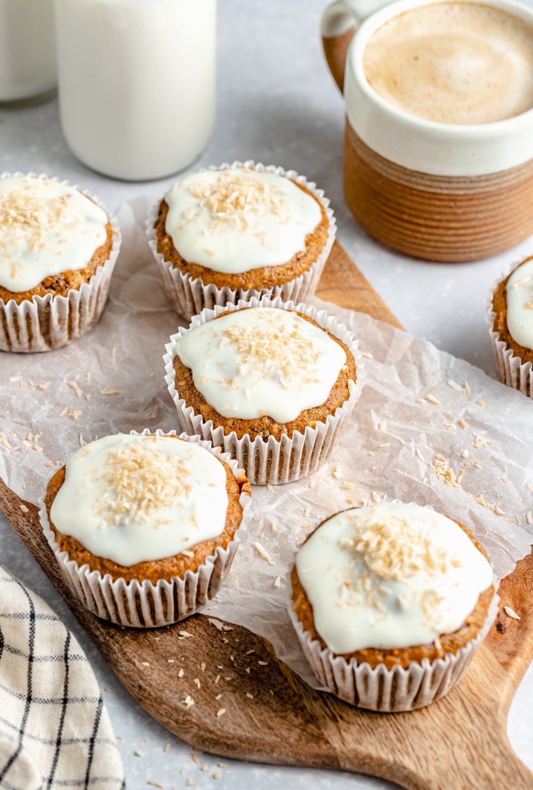 Muffins de pastel de zanahoria saludables rellenos de zanahorias, coco, pasas y nueces. Estos muffins de pastel de zanahoria deliciosamente húmedos están endulzados naturalmente con jarabe de arce puro y compota de manzana. ¡Cubra con un glaseado de queso crema ligero para un refrigerio delicioso o una golosina saludable! Muffins de pastel de zanahoria saludables en una tabla de madera