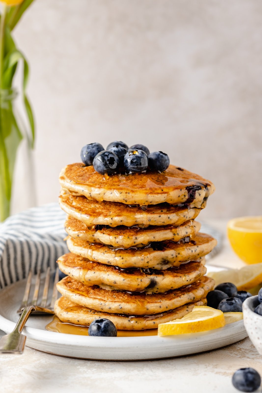 ¡Deliciosos panqueques esponjosos de limón y arándanos con yogur griego para un gran refuerzo de proteínas! Hechos con harina de avena, estos panqueques saludables de limón y arándanos no contienen gluten y están repletos de los sabores brillantes de los arándanos frescos, el jugo de limón y la ralladura. ¡Agregue semillas de amapola para un ambiente primaveral encantador, y no olvide cubrir con bayas adicionales! Montón de panqueques saludables de limón y arándanos