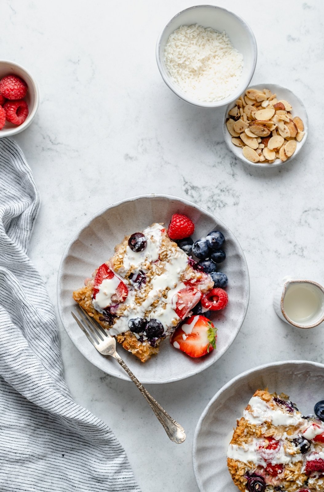 Maravillosa avena horneada con crema y bayas triples hecha con fresas, arándanos y frambuesas y endulzada naturalmente con un toque de jarabe de arce puro. ¡Esta receta fácil de avena horneada con bayas presenta grasas saludables en leche de coco cremosa y es la manera perfecta de usar bayas frescas! Una rebanada de avena horneada con bayas en un plato con bayas