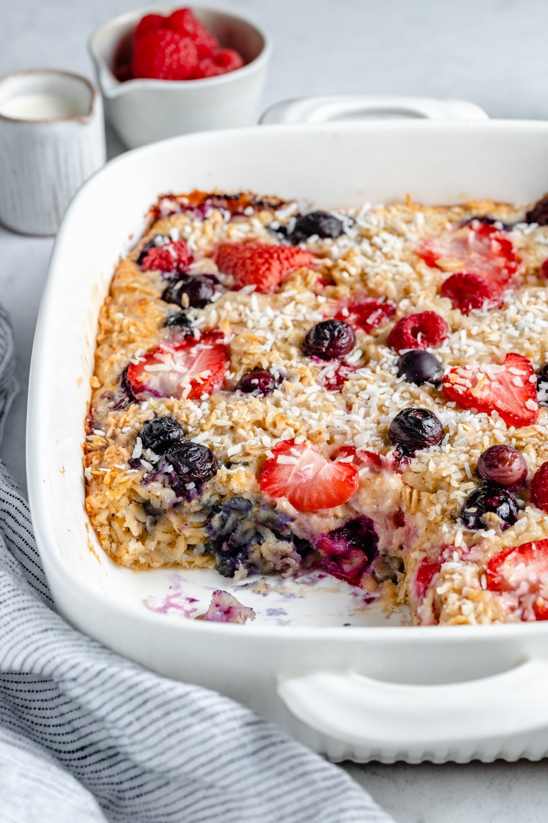 Maravillosa avena horneada con crema y bayas triples hecha con fresas, arándanos y frambuesas y endulzada naturalmente con un toque de jarabe de arce puro. ¡Esta receta fácil de avena horneada con bayas presenta grasas saludables en leche de coco cremosa y es la manera perfecta de usar bayas frescas! Avena horneada con bayas y crema en un molde para hornear, corte una rebanada
